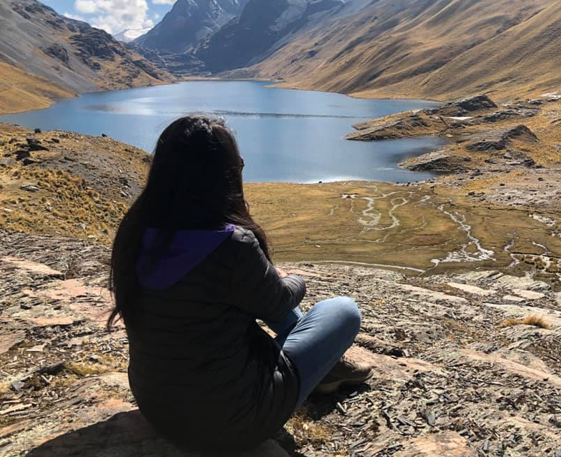 A person sitting on a rock looking at a lake

Description automatically generated