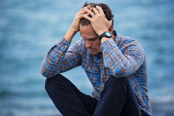 A person sitting on a rock with his hands on his head

Description automatically generated